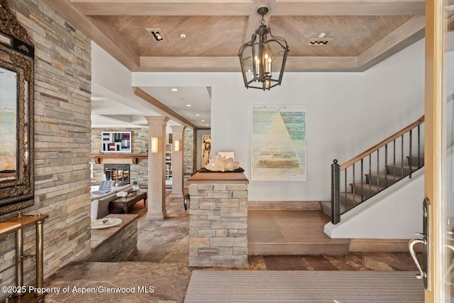 entryway with stairway, wood ceiling, a stone fireplace, a chandelier, and ornate columns