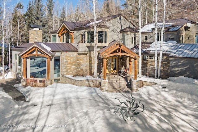 rustic home with stone siding, a standing seam roof, metal roof, and a chimney