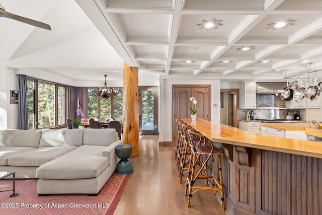 living room with a chandelier, light wood-style flooring, recessed lighting, coffered ceiling, and beamed ceiling