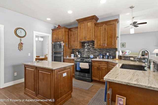 kitchen featuring ceiling fan, appliances with stainless steel finishes, light stone countertops, a kitchen island, and sink