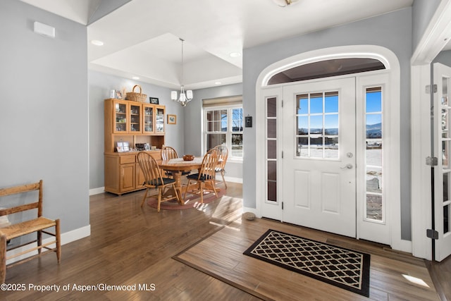 entryway featuring dark wood-type flooring, a raised ceiling, and a notable chandelier