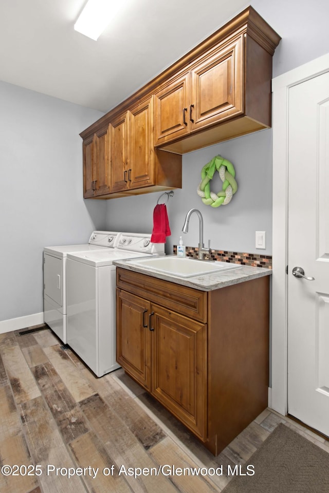 clothes washing area featuring cabinets, sink, light hardwood / wood-style flooring, and independent washer and dryer