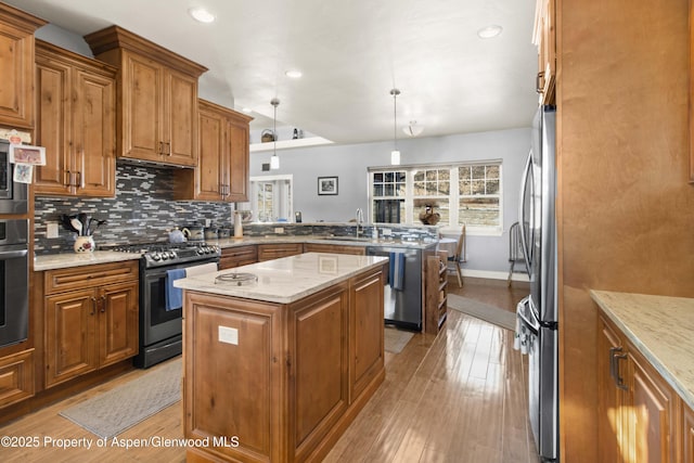 kitchen with kitchen peninsula, appliances with stainless steel finishes, decorative light fixtures, light wood-type flooring, and a kitchen island