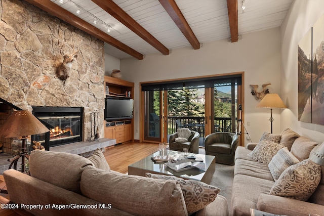 living room featuring rail lighting, wood ceiling, wood-type flooring, beamed ceiling, and a stone fireplace