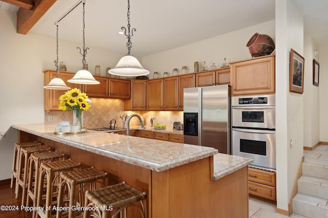 kitchen with kitchen peninsula, appliances with stainless steel finishes, a kitchen bar, light stone counters, and decorative light fixtures