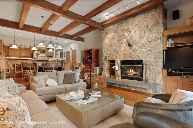 living room with beam ceiling, a stone fireplace, light hardwood / wood-style flooring, and track lighting