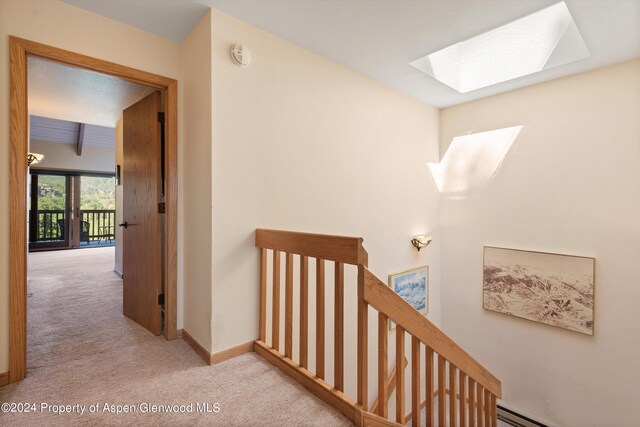 hall featuring beamed ceiling, light colored carpet, a baseboard radiator, and a skylight