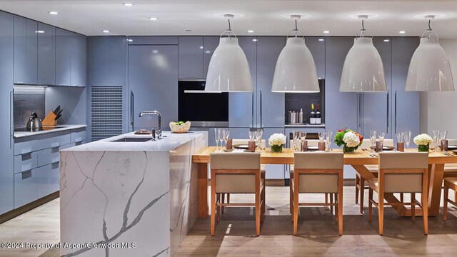 kitchen featuring black electric stovetop, sink, blue cabinetry, decorative light fixtures, and a center island with sink