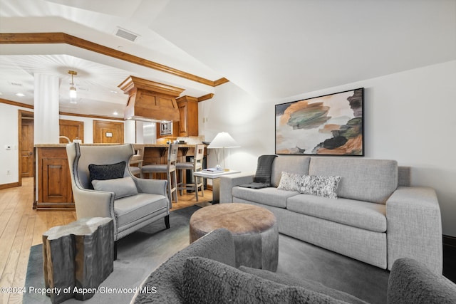 living room featuring lofted ceiling, light wood-type flooring, and ornamental molding