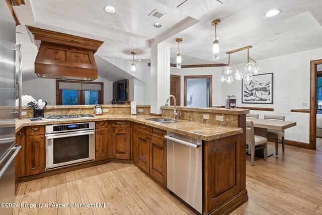 kitchen featuring pendant lighting, sink, light wood-type flooring, custom range hood, and stainless steel appliances