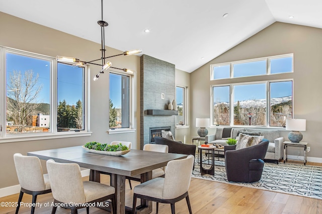 dining area featuring a chandelier, high vaulted ceiling, a fireplace, baseboards, and light wood finished floors