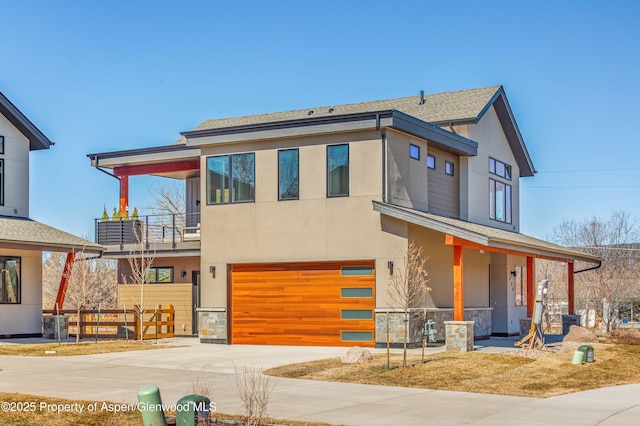 contemporary home with a garage, concrete driveway, a balcony, and stucco siding