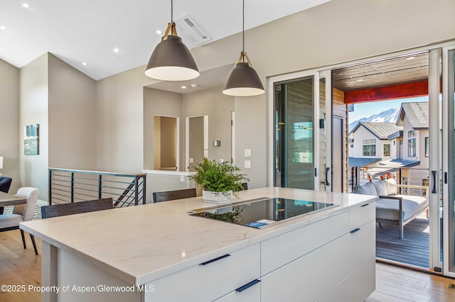 kitchen with decorative light fixtures, light wood-style floors, white cabinetry, light stone countertops, and black electric cooktop