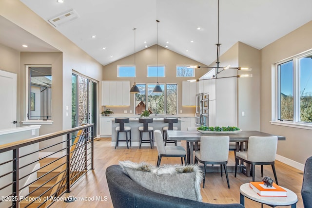 living area with a chandelier, high vaulted ceiling, light wood-style flooring, and visible vents