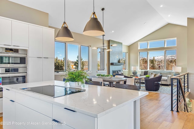 kitchen with stainless steel double oven, black electric cooktop, a fireplace, open floor plan, and light wood-type flooring