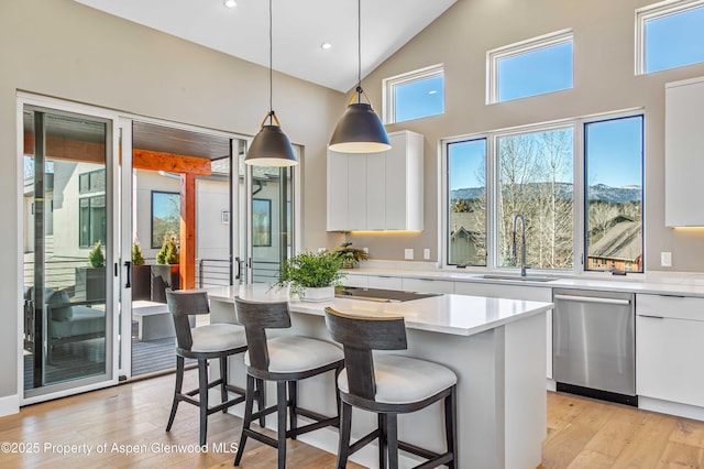 kitchen featuring dishwasher, light wood-type flooring, a kitchen bar, white cabinetry, and a sink