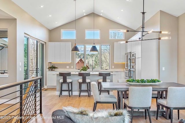 dining area featuring baseboards, light wood-style flooring, high vaulted ceiling, a notable chandelier, and recessed lighting