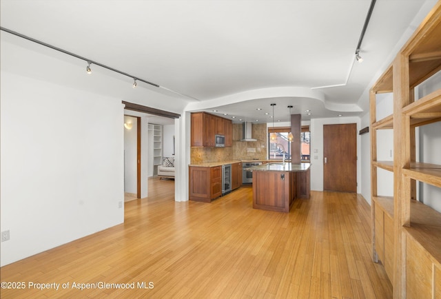 kitchen with wall chimney range hood, brown cabinets, tasteful backsplash, and light wood-style flooring