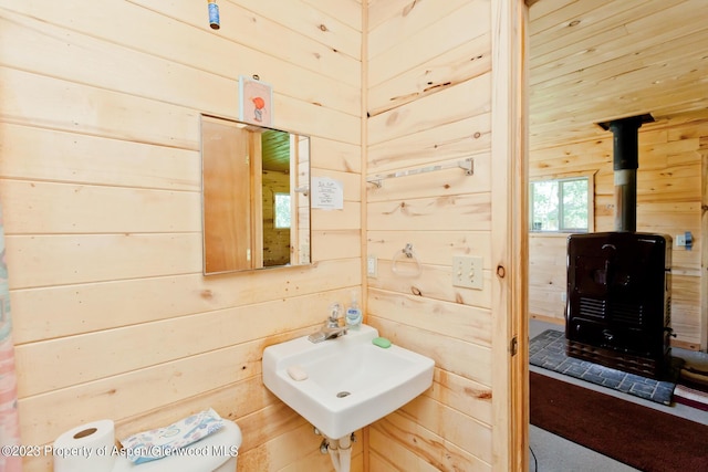 bathroom featuring toilet, a wood stove, wooden walls, and sink