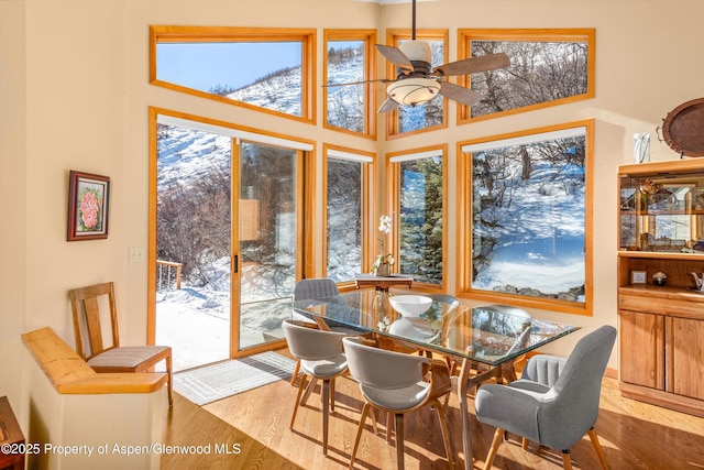 dining space with a towering ceiling, wood-type flooring, and ceiling fan