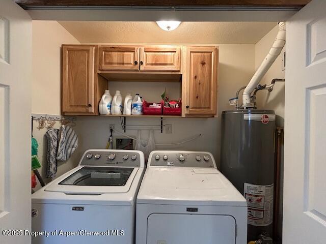 clothes washing area with washing machine and clothes dryer, water heater, and cabinet space