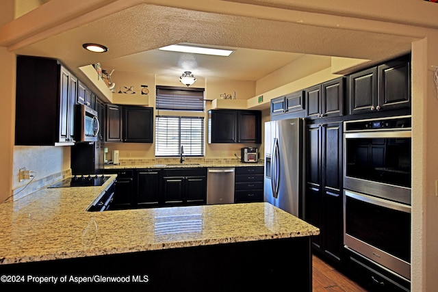 kitchen with kitchen peninsula, light stone countertops, sink, and stainless steel appliances