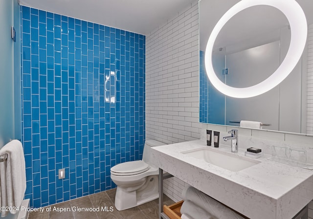 bathroom featuring tile patterned flooring, toilet, sink, and tile walls