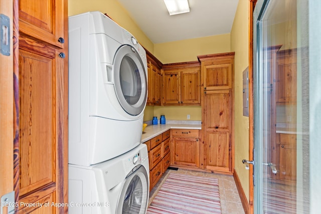 laundry area featuring cabinets, stacked washer / drying machine, and light tile patterned floors