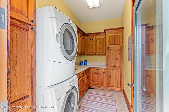 laundry room featuring cabinet space, stacked washer / dryer, and light tile patterned flooring