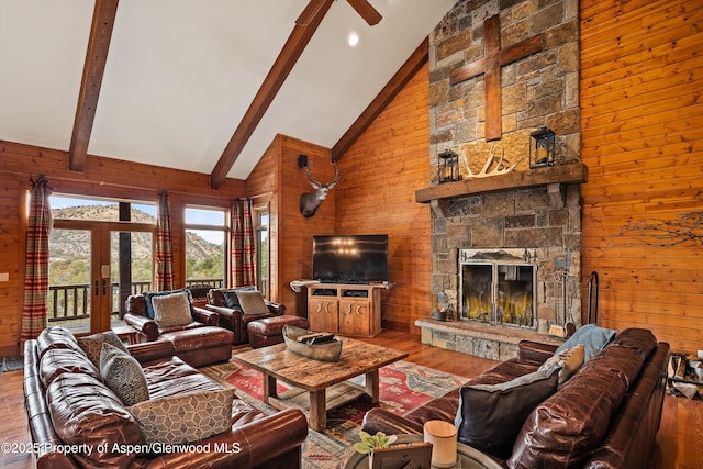 living room with a stone fireplace, high vaulted ceiling, wooden walls, beamed ceiling, and hardwood / wood-style flooring