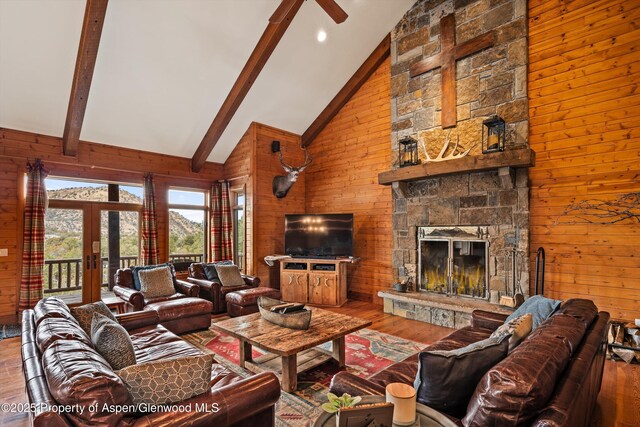 living room with wooden walls, wood finished floors, a stone fireplace, high vaulted ceiling, and beam ceiling