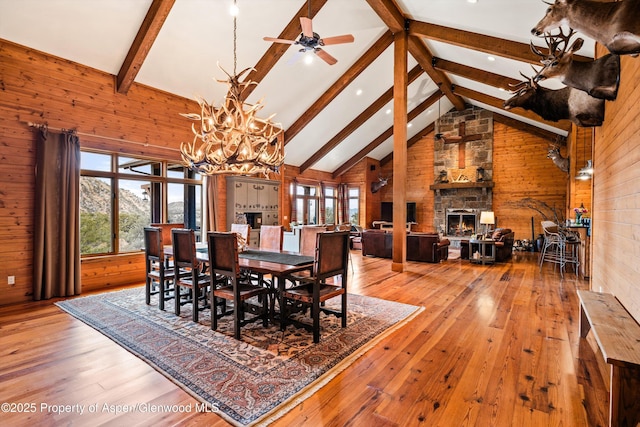 dining room with a stone fireplace, wood walls, high vaulted ceiling, light wood-type flooring, and beamed ceiling