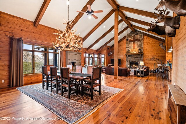 dining room with beam ceiling, wood-type flooring, wood walls, a stone fireplace, and high vaulted ceiling