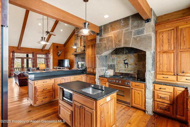 kitchen with dark countertops, appliances with stainless steel finishes, open floor plan, vaulted ceiling with beams, and a sink