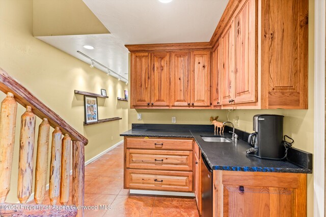 kitchen featuring brown cabinets, light tile patterned floors, dark countertops, rail lighting, and a sink