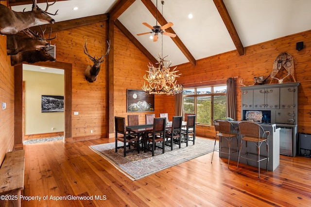 dining space with beam ceiling, high vaulted ceiling, light wood-type flooring, and wooden walls