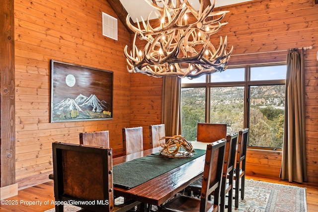 dining room with high vaulted ceiling, wooden walls, a chandelier, and light hardwood / wood-style flooring