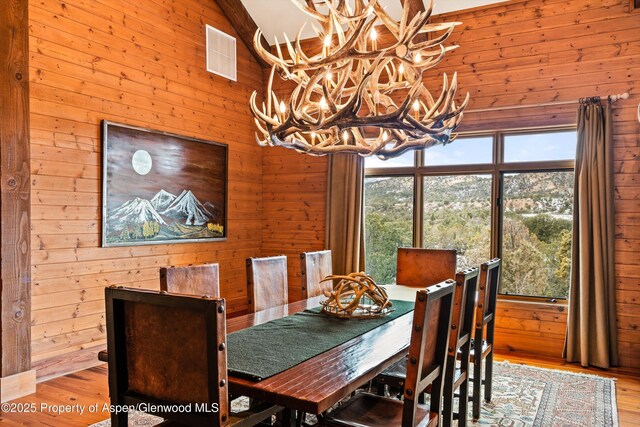 dining area with a notable chandelier, visible vents, wood walls, wood finished floors, and high vaulted ceiling