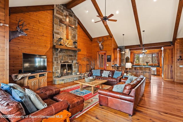 living room featuring beam ceiling, wooden walls, high vaulted ceiling, a fireplace, and light hardwood / wood-style floors