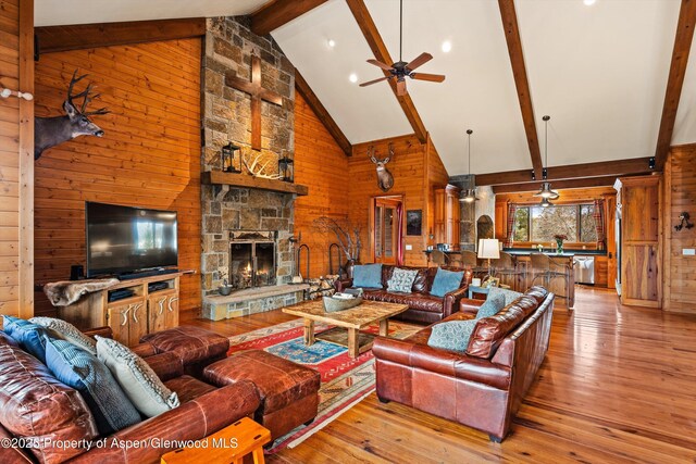 living area with high vaulted ceiling, a stone fireplace, wooden walls, beam ceiling, and wood-type flooring