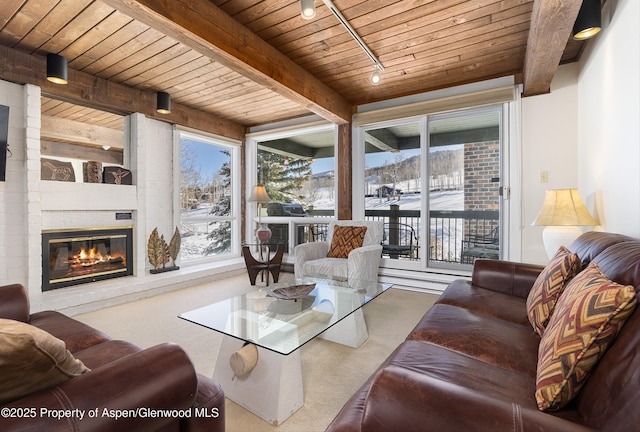 carpeted living room featuring beamed ceiling, rail lighting, a brick fireplace, and wood ceiling