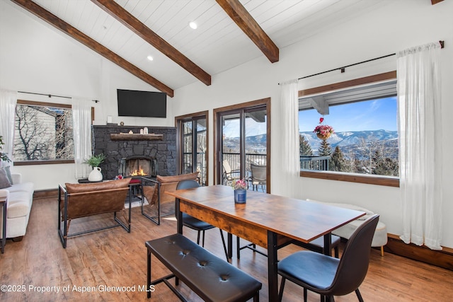 dining area featuring high vaulted ceiling, a fireplace, beamed ceiling, light hardwood / wood-style floors, and wood ceiling