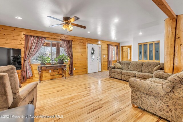 living room with ceiling fan, light hardwood / wood-style floors, and wooden walls