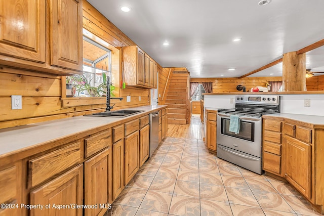 kitchen with appliances with stainless steel finishes, sink, wooden walls, and light tile patterned flooring