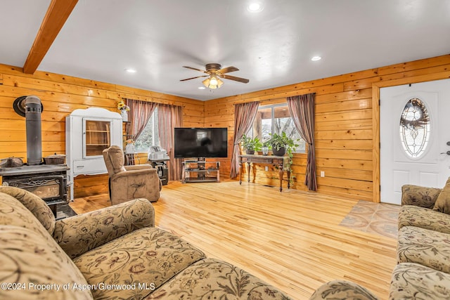 living room with a wood stove, ceiling fan, and wooden walls