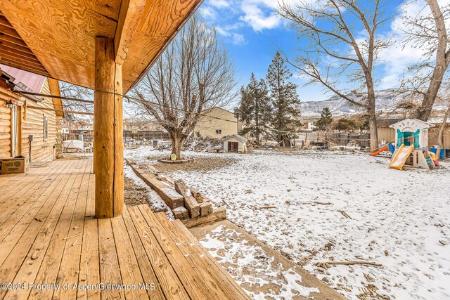 yard covered in snow with a playground and a deck with mountain view