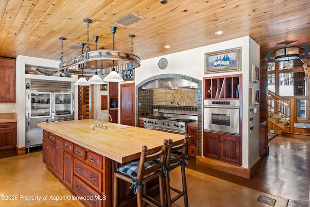 kitchen featuring tasteful backsplash, premium appliances, a sink, butcher block counters, and finished concrete flooring