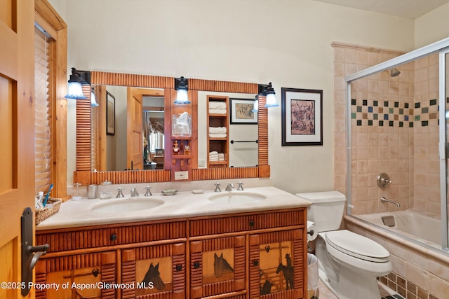 full bathroom featuring a sink, bath / shower combo with glass door, double vanity, and toilet