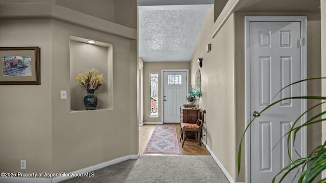 foyer with light colored carpet, a textured ceiling, and baseboards