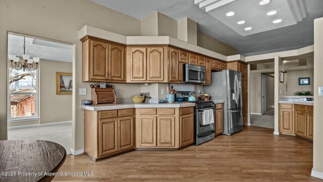 kitchen with brown cabinetry, wood finished floors, stainless steel appliances, light countertops, and a chandelier